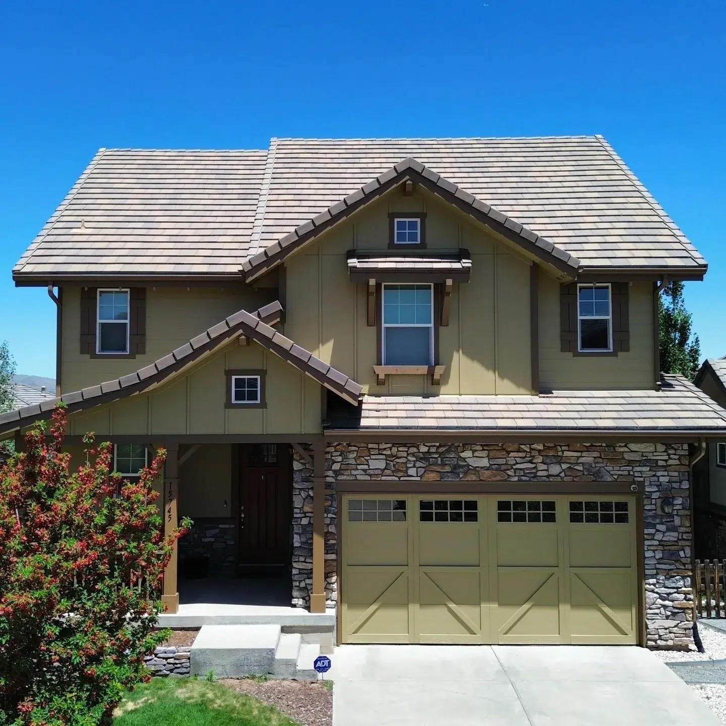 Sage Green Two-Story Residential Home Sage green and taupe two-story residential home with gray roof, stone garage base, sage-painted garage doors, and brown wood