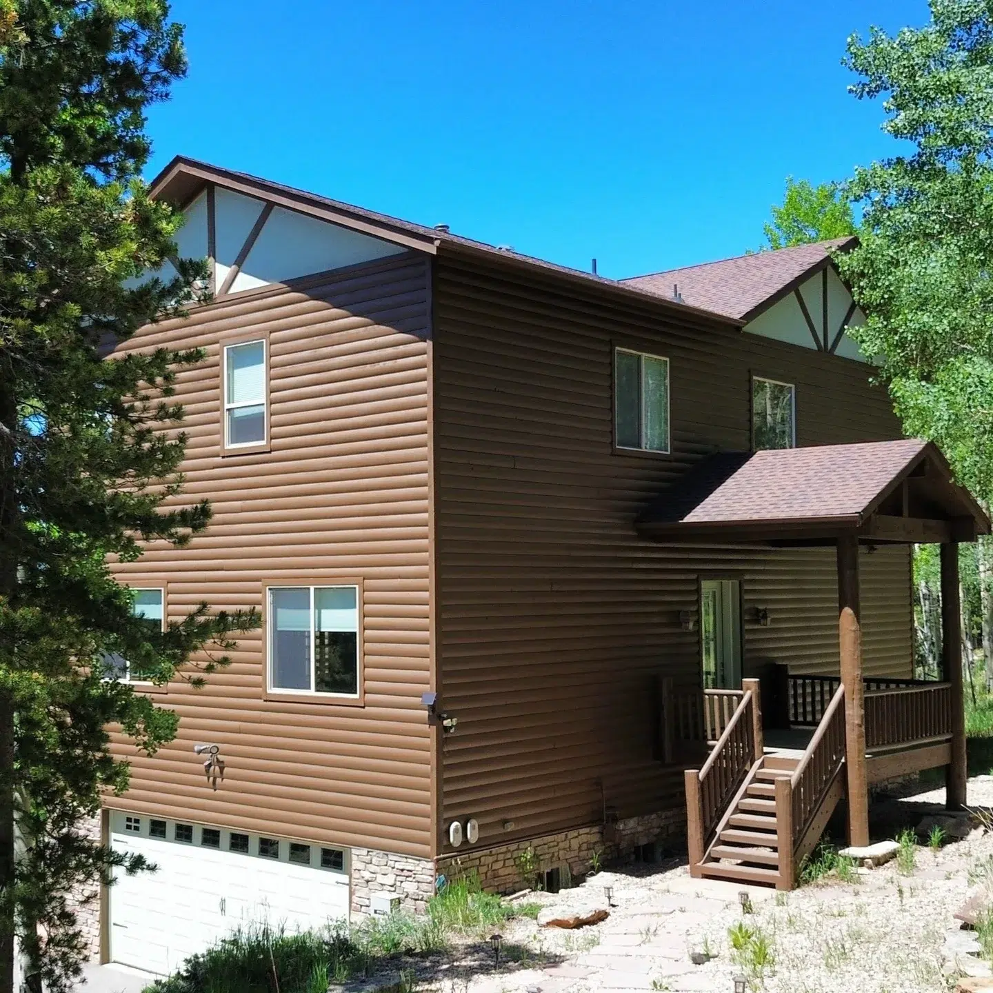 Tan and Dark Brown Residential Exterior Two-story residential home with tan log-style siding on left, dark brown horizontal siding on right, wood deck with stairs