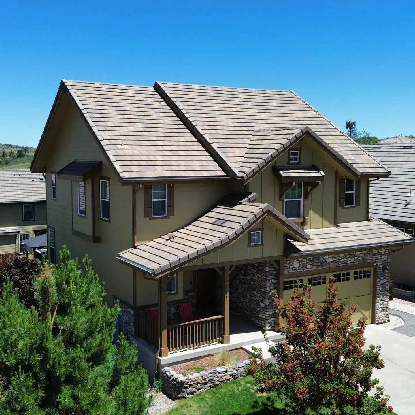 Tan Two-Story Residential Home Exterior Tan two-story residential home with stone garage base, tan garage doors, slate-gray roof, and wooden front porch railing in